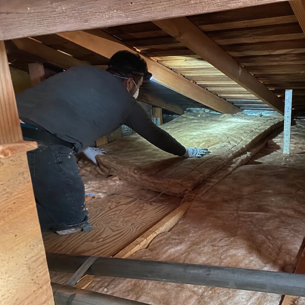 Professional installing fiberglass batt insulation in a residential attic