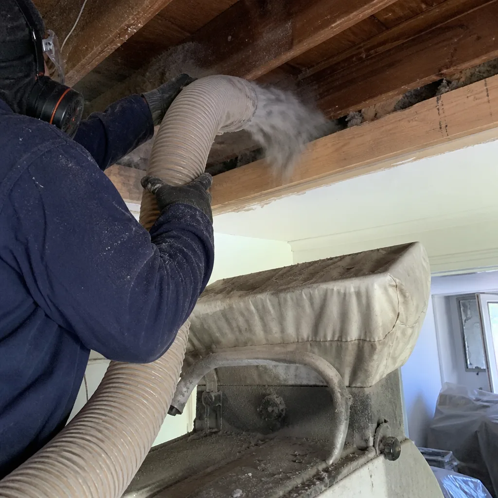 Technician installing blown-in insulation into a ceiling joist space